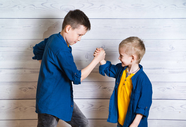Happy and friendly brothers during the game in studio. Two positive friends fighting by hands isolated on the wooden wall background. Happy childhood with emotions and energy. - Valokuva, kuva