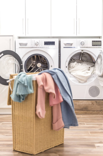 Cesta de lavanderia com roupas sujas com máquinas de lavar e secar no fundo
 - Foto, Imagem