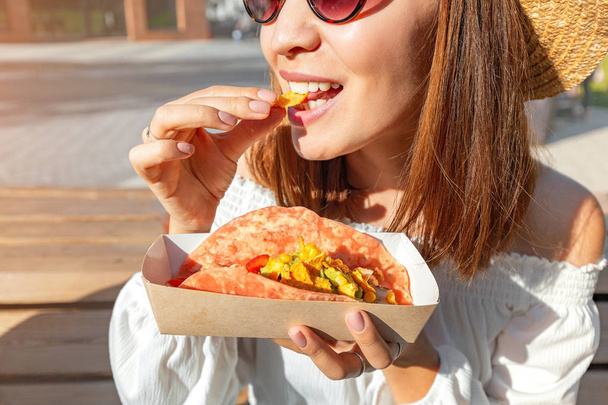 Happy asian girl eating taco outside. Mexican fastfood cuisine. Tasty and spicy snack in park - Photo, Image