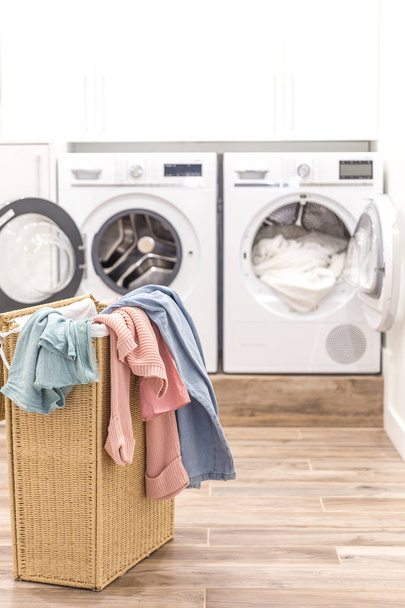 Pyykkikori likaisilla vaatteilla, taustalla pesu- ja kuivauskoneet
 - Valokuva, kuva