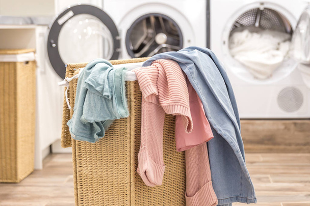 Pyykkikori likaisilla vaatteilla, taustalla pesu- ja kuivauskoneet
 - Valokuva, kuva
