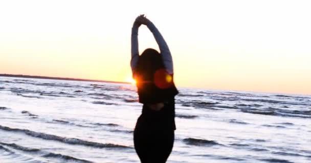 Młoda kobieta na tle zachodu słońca słońce na wybrzeżu robi ćwiczenia wykonywane przez bieganie, rozciąganie i opadanie, Dziewczyna na morzu uprawia jogę. Portret: Wolny ruch, Zachód słońca. - Materiał filmowy, wideo