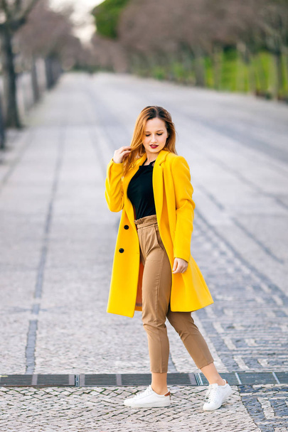 giovane donna in cappotto giallo guardare in basso. Moda di strada. città
 - Foto, immagini