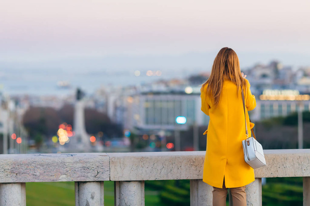 дівчина в жовтому пальто з сумочкою біля паркану з видом на огорожу
  - Фото, зображення