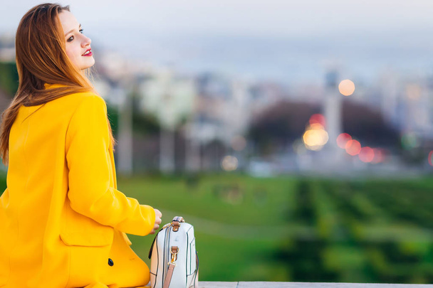Nuori nainen keltaisessa takissa istuu ja käsilaukku vieressään. e
 - Valokuva, kuva