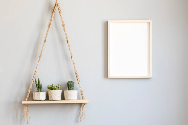 Stylish and minimalistic scandinavian interior with mock up poster frame and hanging wooden shelf with beautiful succulents in cement pots. Modern home decor. Gray background wall. Real photo. - Фото, зображення