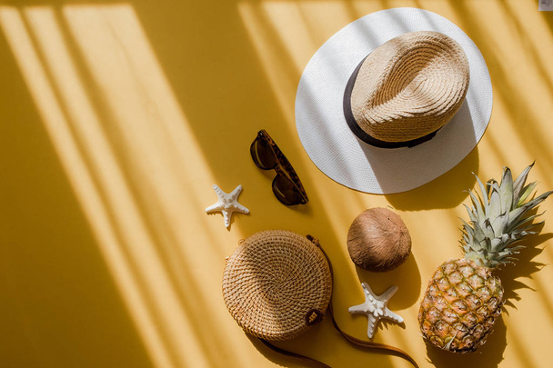 farbenfrohe Sommer-Damenmode flach lag. Strohhut, Bambusbeutel, Sonnenbrille, Kokosnuss, Ananas auf gelbem Hintergrund - Foto, Bild