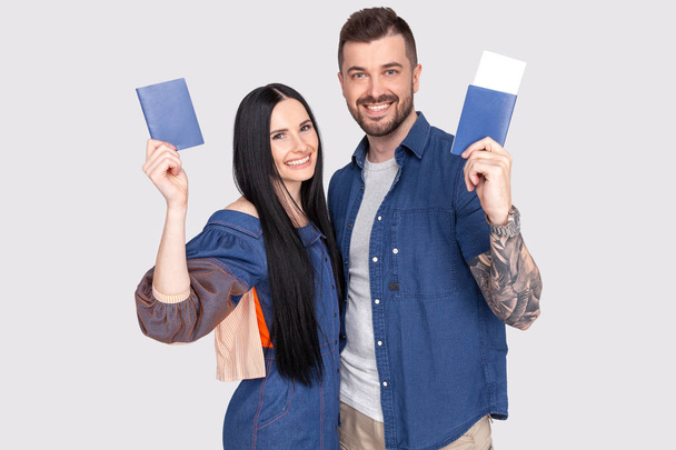 Portrait of joyful glad couple holding passport with flying tickets in hands looking at camera isolated on bright grey background - Фото, изображение