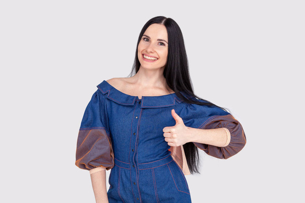 Portrait of supportive pleased and delighted female customer in jeans dress sharing positive feedback showing thumbs up gesture thrilled and satisfied smiling, liking idea or product, cheering - Photo, Image
