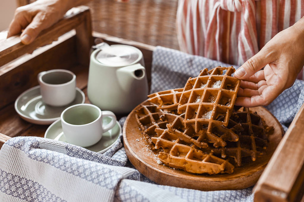Women holds fresh baked waffles and tea mugs for breakfast. Morn - 写真・画像
