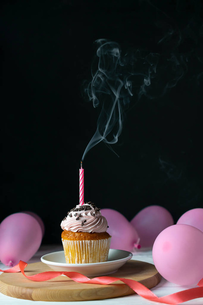 Happy birthday cupcake with a candle blown out on a black background with balloons - Photo, image