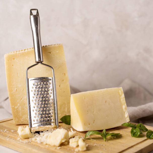 Grated italian parmesan cheese on wooden chopping board with a block of parmasan and a grater in the background. - 写真・画像