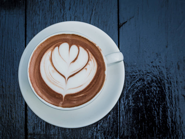 Kahvikuppi lehdet muoto latte art vaahto musta puu pöytä aamulla ennen työn aloittamista virkistää
.  - Valokuva, kuva