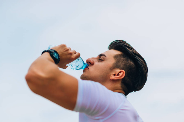 Sporty caucasian man drinking water after crossfit training - Foto, afbeelding
