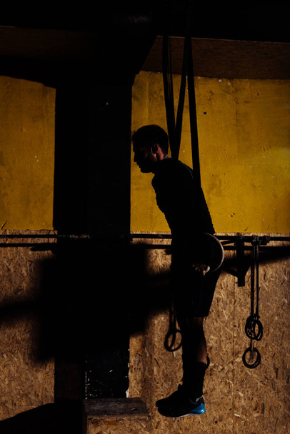 Silhueta de jovem homem apto puxando para cima em anéis de ginástica
 - Foto, Imagem