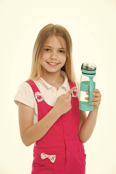 Stay hydrated. Girl cares about health and water balance. Girl on smiling face posing with water bottle isolated white background. Kid girl with long hair pointing at bottle. Water balance concept - Фото, изображение
