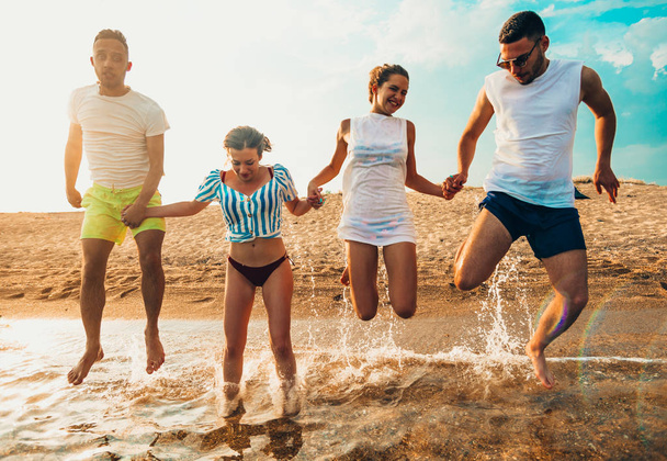 Gente divertida saltando en el mar al atardecer
 - Foto, imagen