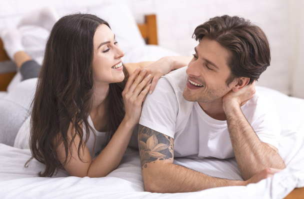 Happy millennial couple lying in bed, planning weekend - Zdjęcie, obraz
