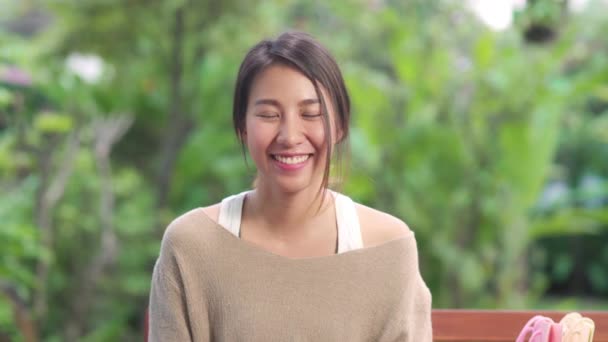 Ázsiai nő érzés boldog mosolygós és keresi a kamera, miközben pihenjen az asztalon kertben otthon reggel. Életmód nők pihenni otthon koncepció.  - Felvétel, videó