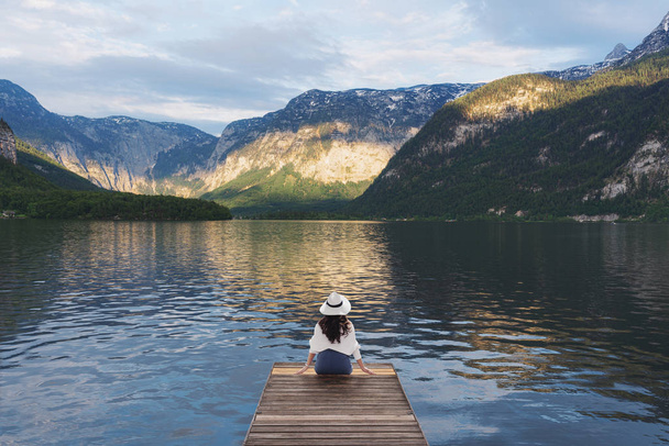 Young woman sitting alone on wooden pier, looking lake and mountain view in summer at Hallstatt, Austria - Фото, изображение