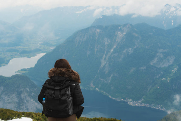 a girl with backpack looking beautiful aerial view of mountains and Hallstatt city in Austria in summer - Photo, Image