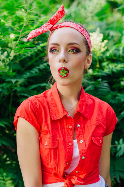 Beautiful young pin up girl with bright make up and fresh natural strawberry in mouth. - Φωτογραφία, εικόνα