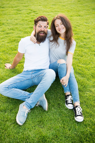 Man bearded hipster and pretty woman in love. Summer vacation. Emotional couple radiating happiness. Love story. Couple relaxing green lawn. Happy together. Couple in love cheerful youth booth props - Photo, Image