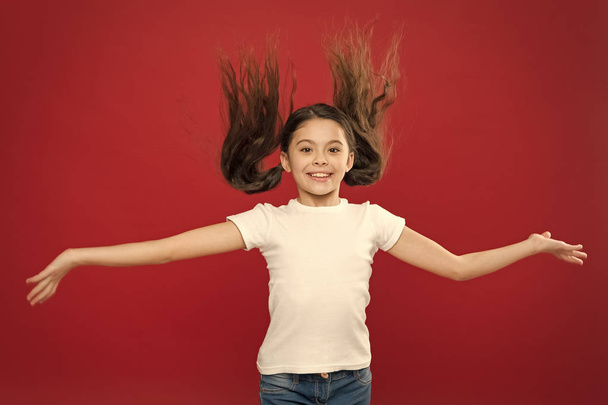 Kid smiling cute face live carefree happy life. Enjoy every moment. Young and free. Happy child girl with long hair on red background. Happiness and joy. Positive emotions. Child care and upbringing - Zdjęcie, obraz
