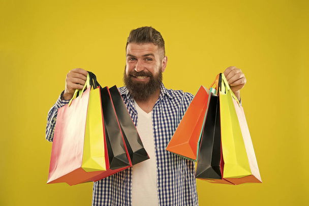 Man bearded hipster cheerful face carry paper shopping bags on yellow background. Enjoy shopping profitable deals black friday. Shopping with discount enjoy purchase. Make shopping more joyful - Фото, изображение