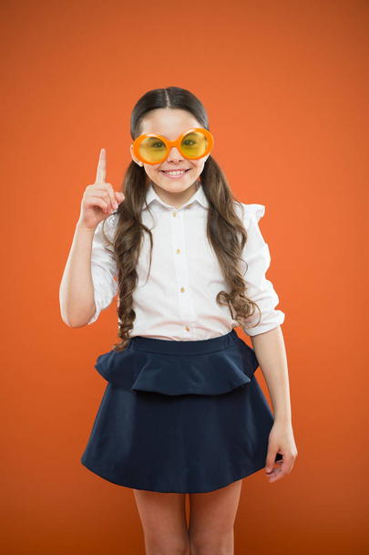 Funny idea. Little girl in funny glasses pointing finger up on orange background. Funny child wearing sunglasses with color filter. My eyes go funny - Fotografie, Obrázek