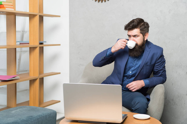 Drinking coffee for breakfast. Businessman drinking coffee at workplace. Bearded man holding drinking cup at laptop. Enjoy drinking tea or other hot beverage - Foto, Imagem