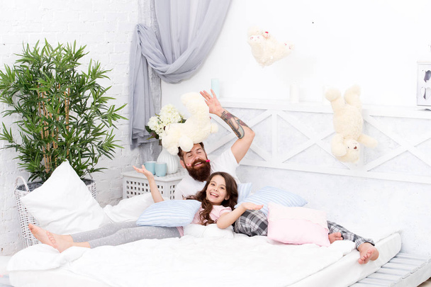 Having fun pajamas party. Slumber party. Happy fatherhood. Ending of crazy evening. Dad and girl relaxing bedroom. Pajamas style. Father bearded man funny hairstyle ponytails and daughter in pajamas - 写真・画像