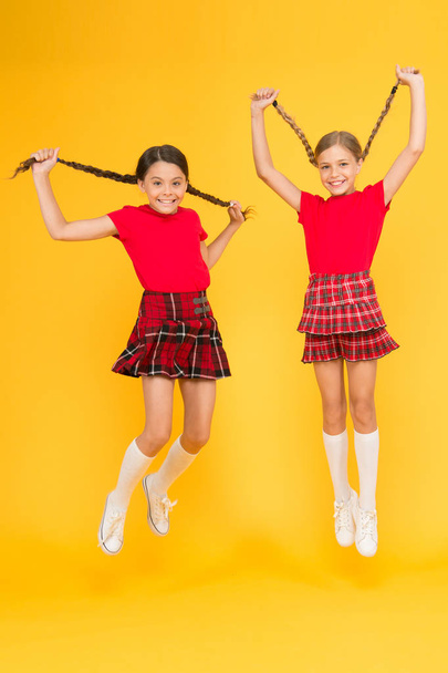 Join celebration. School uniform. Scottish style. Cheerful friends schoolgirls jumping yellow background. Celebrate holiday. Scottish holiday. Kids girl wear checkered dresses. National holiday - Φωτογραφία, εικόνα