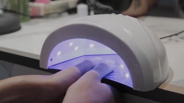 Молода дівчина сушить лак для нігтів під ультрафіолетовою лампою в манікюрному салоні
. - Кадри, відео
