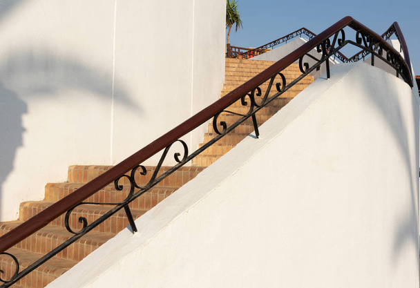 dřevěné zábradlí s kovovou výzdobou, prvek, detail schodiště proti pozadí cihlových schodů a bílá zeď vně - Fotografie, Obrázek
