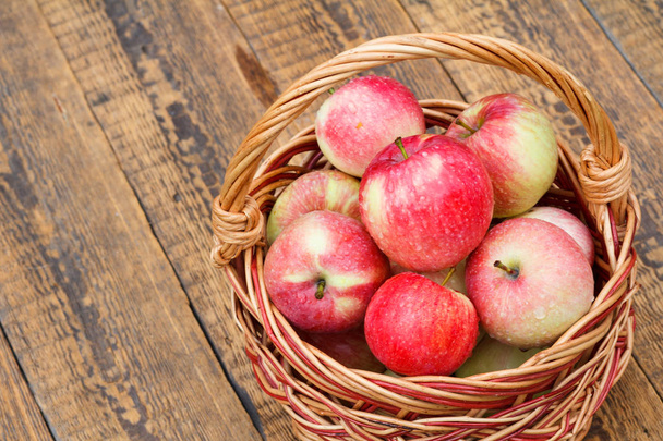 Красные яблоки в плетеной корзине на деревянных досках
 - Фото, изображение