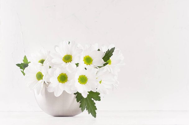 Fresh spring chamomile bouquet with leaves in silver modern vase on white wood table and soft light background. - Foto, immagini