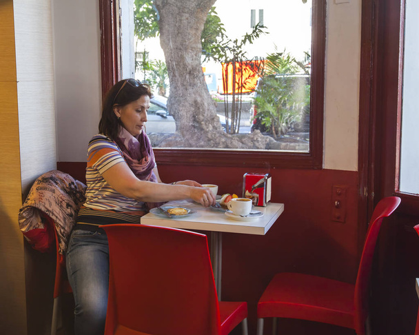 Las-Palmas de Gran Canaria, Spain, on January 8, 2018.  The attractive woman has coffee at a table inside small picturesque cafe - Fotó, kép