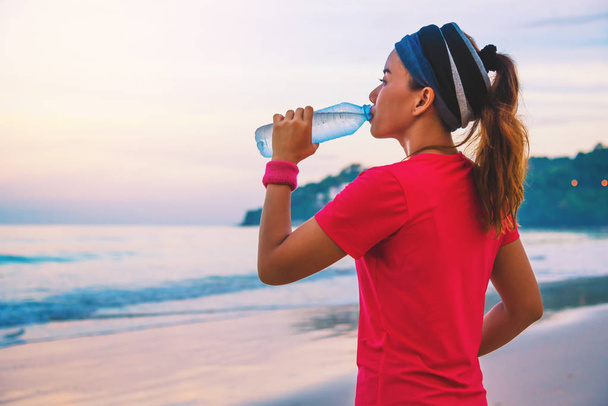 Asian women jogging workout on the beach in the morning. Relax with the sea walk and drinking water from the plastic bottles. beach, sport, exercise, travel Thailand. - Photo, Image
