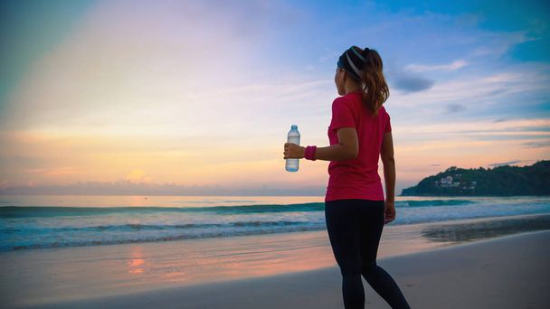 Aasialaiset naiset lenkkeilemässä rannalla aamulla. Rentoudu merikävely ja juomavesi muovipullot. ranta, urheilu, liikunta, matkailu Thaimaa
. - Valokuva, kuva