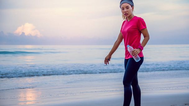 Mujeres asiáticas haciendo ejercicio en la playa por la mañana. Relájese con el paseo marítimo y beba agua de las botellas de plástico. Correr en la playa
. - Foto, Imagen