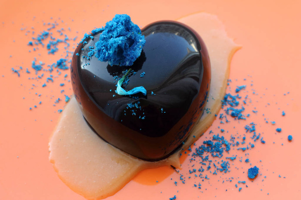 Postre en forma de corazón con pétalo azul y decoraciones sobre fondo naranja
 - Foto, imagen