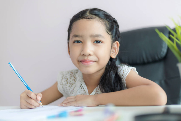 鉛筆を使って紙に書く小さなアジアの女の子は、hをやって - 写真・画像
