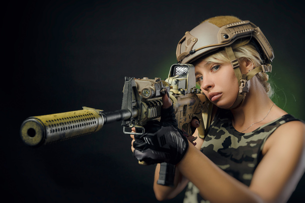 dívka ve vojenských předevkích s pistolí v ruce na tmavém pozadí v oparu - Fotografie, Obrázek