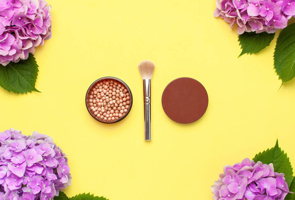 Set of decorative cosmetics makeup brushes, blush face balls, pink hydrangea flowers on yellow background top view Flat lay copy space. Beauty blogger concept. Fashion background. Makeup accessories - Photo, Image