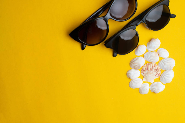 Summer accessories, shells and couple sun glasses on yellow back - Foto, imagen
