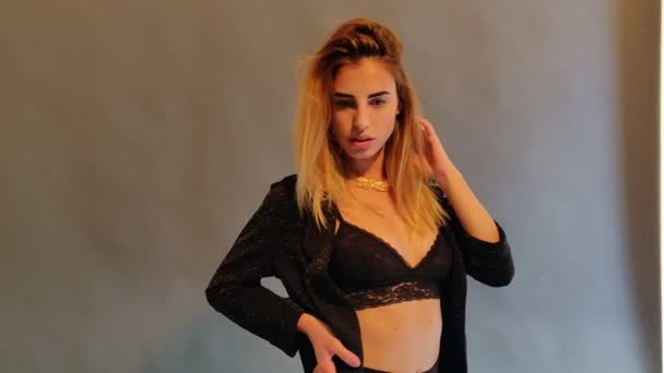 Jonge blonde vrouw in zwarte lingerie poseren en broek poseren op beige achtergrond  - Video