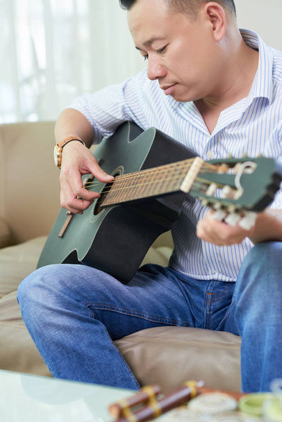 Uomo seduto sul divano a casa e studiare per suonare la chitarra nel suo tempo libero
 - Foto, immagini