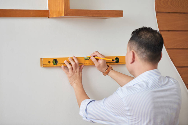 Hombre haciendo reparadores a sí mismo en la casa, comprobando la uniformidad de la pared blanca usando el nivel
 - Foto, Imagen