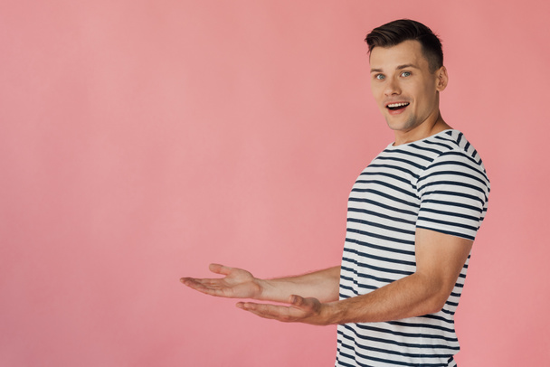 smiling man in striped t-shirt pointing with hands isolated on pink - Foto, afbeelding